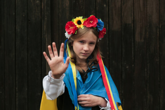 Stop war in Ukraine.Blond crying girl with Ukrainian flag showing stop with her hand.Peace in Ukraine concept.